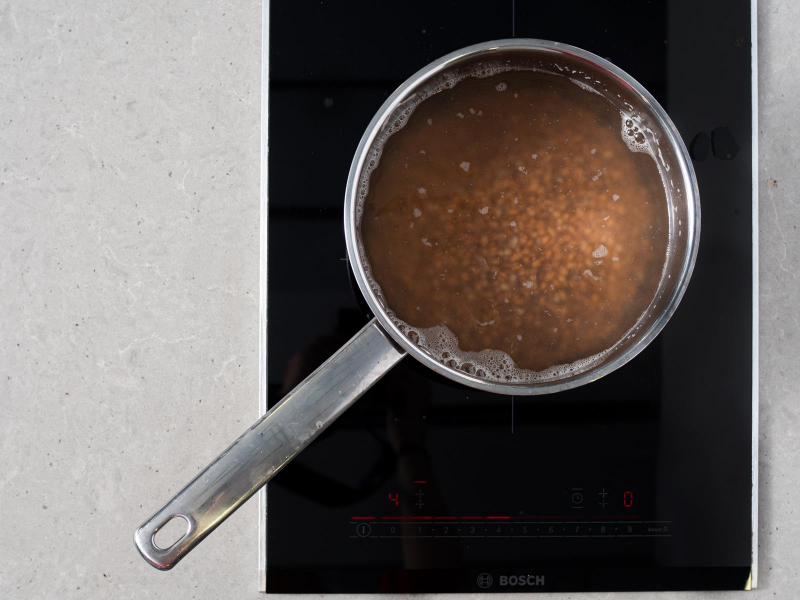 Gotujące się ziarna pszenicy w rondelku na palniku kuchenki