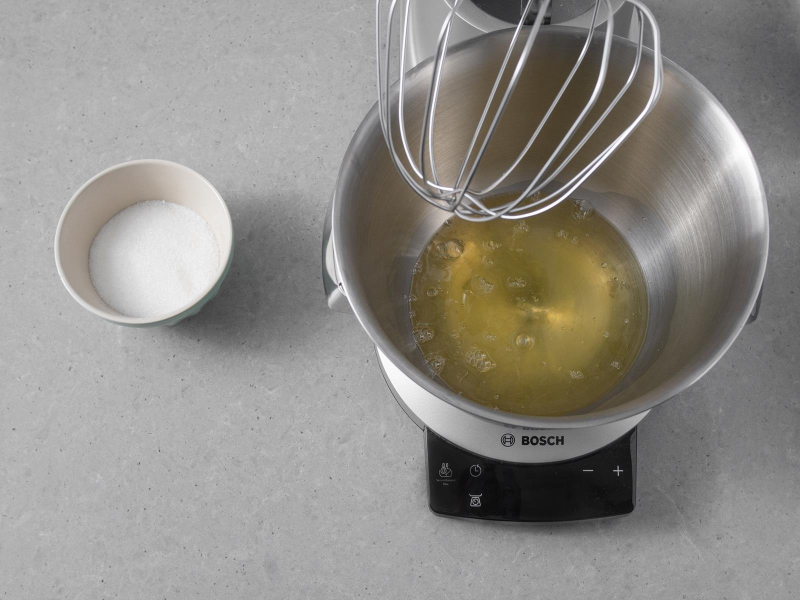 Białka w misie miksera firmy Bosch. Obok w miseczce cukier.
