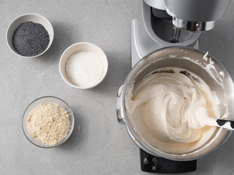 W misie miksera bosch masa na biszkopt do makowej panienki. Obok w osobnych miseczkach mak, zmielone migdały oraz wiórki kokosowe.