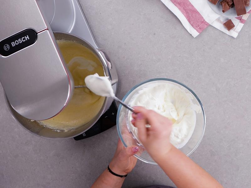 dodawanie twarogu sernikowego do misy robota kuchennego bosch zawierającej masę z utartego masła, cukru pudru, żółtek, mleka, cukru z wanilią i mleka w proszku