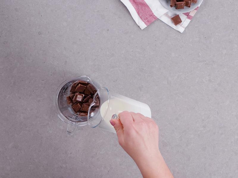 do szklanego naczynia z połamaną na kawałki czekoladą jest przelewana gorąca śmietanka