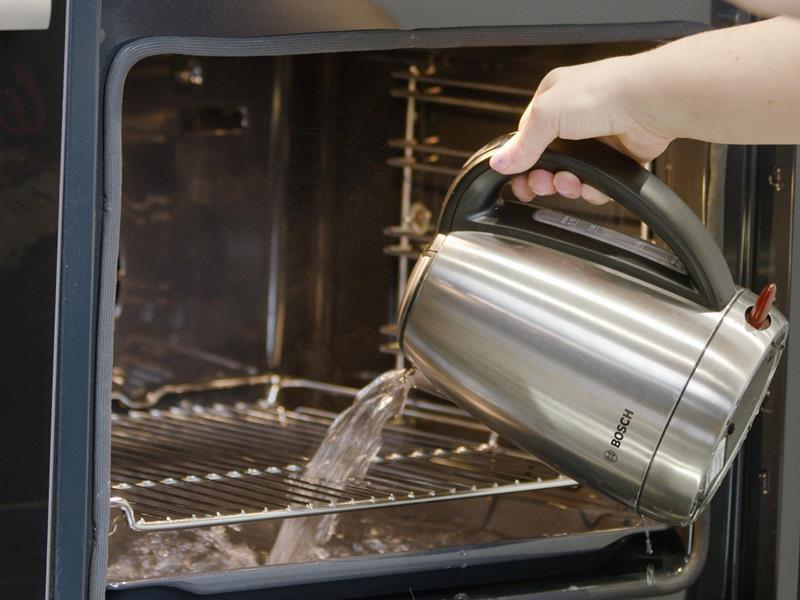 przelewanie wrzątku na blachę na dnie piekarnika do zaparowania go w celu pieczenia sernika w kąpieli wodnej