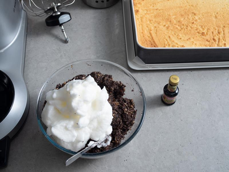 masa makowa w szklanej misce z dodanymi ubitymi białkami, obok opakowanie ekstraktu migdałowego dr. oetkera oraz upieczone kruche ciasto w formie do pieczenia