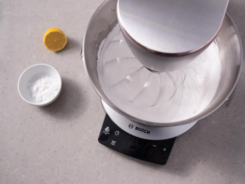 w misie robota kuchennego bosch ubijanie bia艂ek z cukrem na bez臋, obok miseczka ze skrobi膮 ziemniaczan膮 oraz p贸艂 cytryny