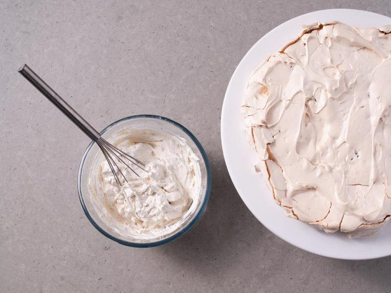 w szklanej miseczce z trzepaczk膮 kuchenn膮 krem kawowy do tortu dak艂as, obok blat bezowy na paterze