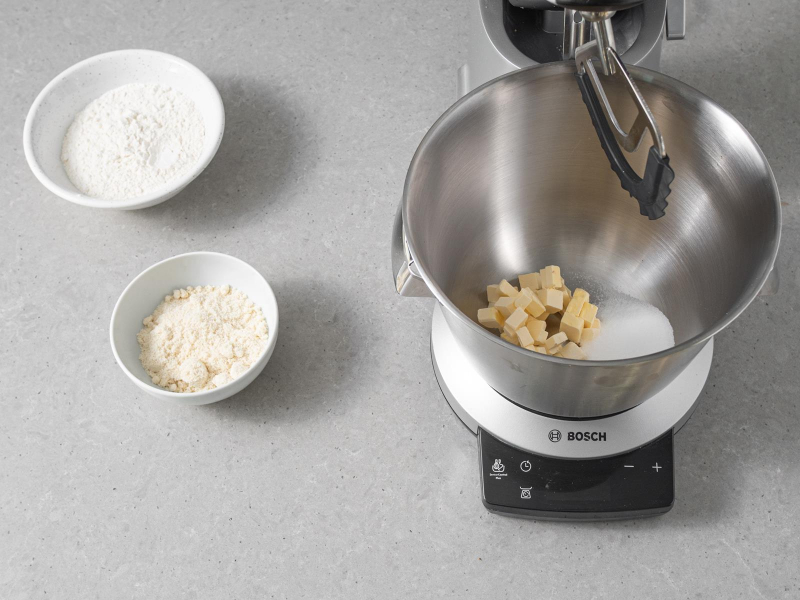 W misie miksera firmy Bosch cukier z margaryną roślinną. Obok mąka pszenna oraz mąka migdałowa w osobnych miseczkach.