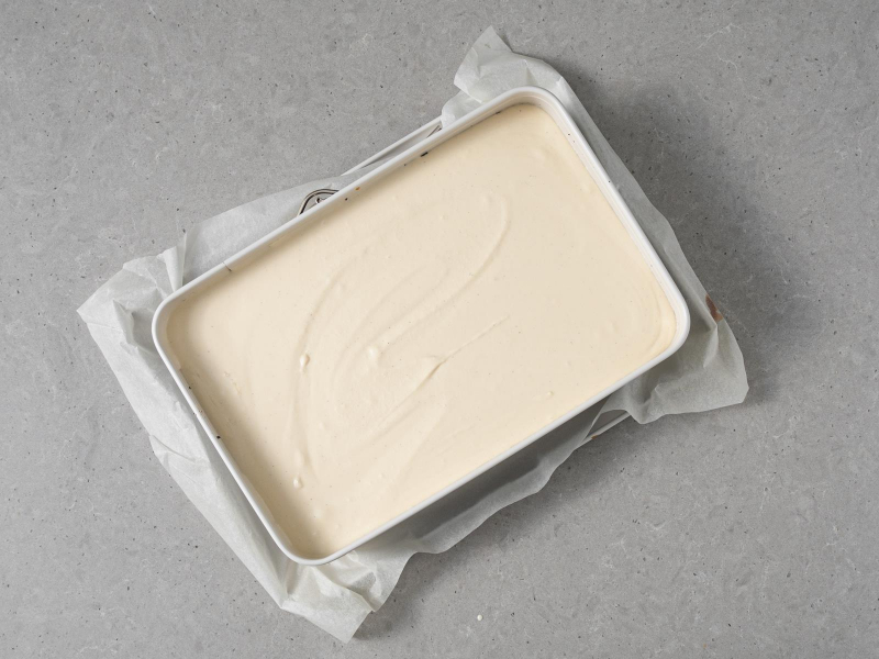 Masa tofurnikowa wyłożona na masę makową w formie do pieczenia.