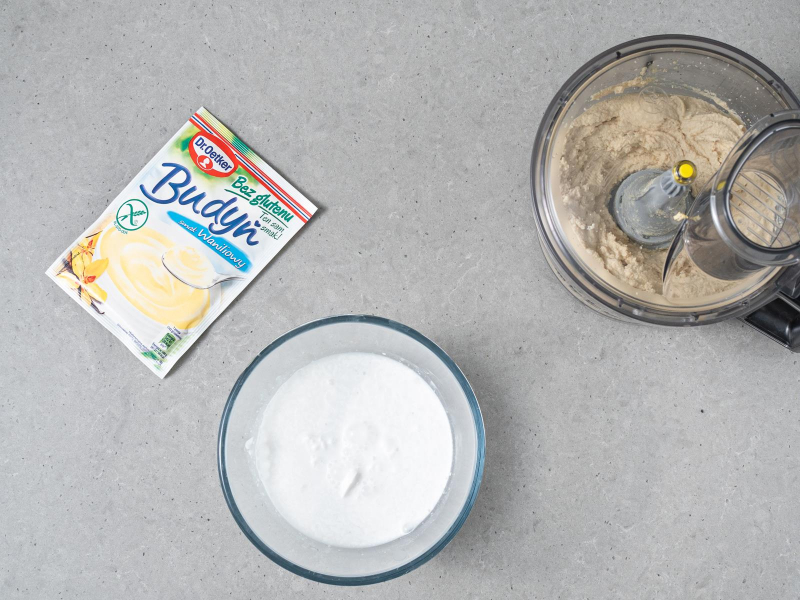 Zblendowane tofu w malakserze. Obok mleczko kokosowe w miseczce oraz opakowanie budyniu waniliowego dr. oetkera.