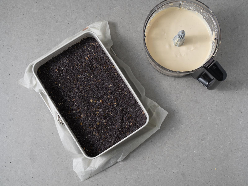 Masa makowa wyłożona na kruchym spodzie. Obok masa tofurnikowa w malakserze.