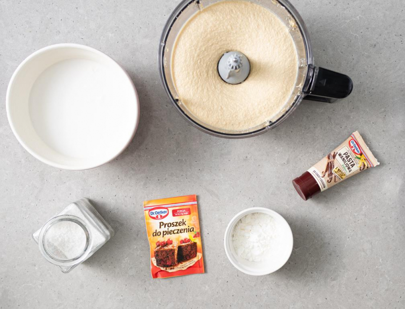 Zblendowana masa tofurnikowa z malakserze. Obok proszek do pieczenia Dr. Oetkera i pasta waniliowa Dr. Oetkera. W miseczkach mleczko kokosowe, skrobia kukurydziana i sól.