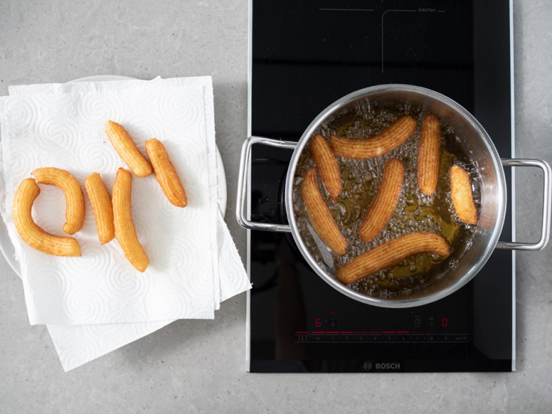 Smażenie churros w garnku. Obok usmażone churros na ręczniku papierowym.