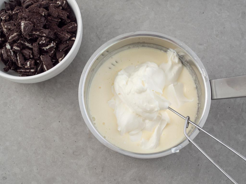 w rondelku śmietanka z jogurtem obok połamane ciasteczka oreo