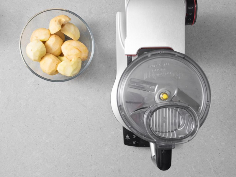 Jabłka w misce. Obok robot kuchenny firmy Bosch z przystawką krojącą.