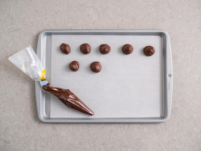 ganache wyciskany na papierze do pieczenia na płaskiej prostokątnej blaszce za pomocą rękawa cukierniczego z odciętą końcówką