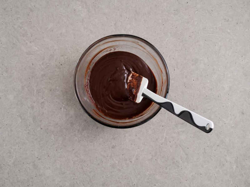 czekolada rozpuszczona z masłem i śmietanką w szklanej miseczce z silikonową szpatułką kuchenną