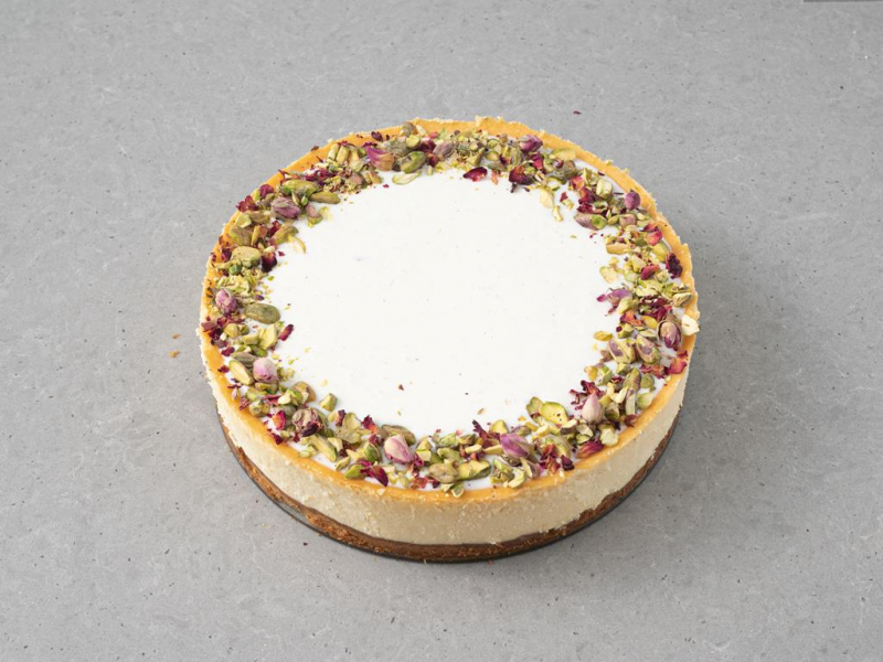 Sernik z pistacjami udekorowany polewą ze śmietanki, pistacjami i płatkami róży.