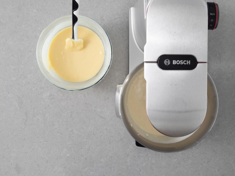 W misie robota kuchennego masa serowa. Obok biała czekolada zalana śmietanką.