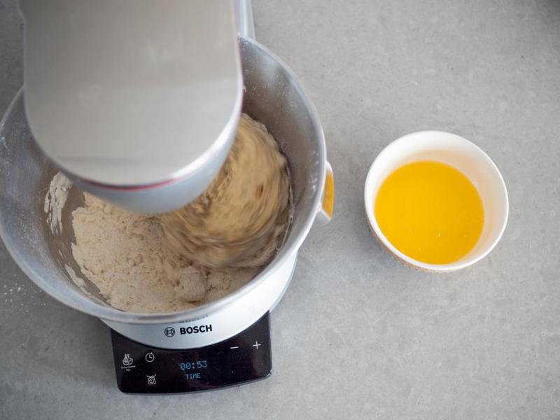 w misie miksera wyrabiane ciasto drożdżowe, obok miseczka z roztopionym masłem