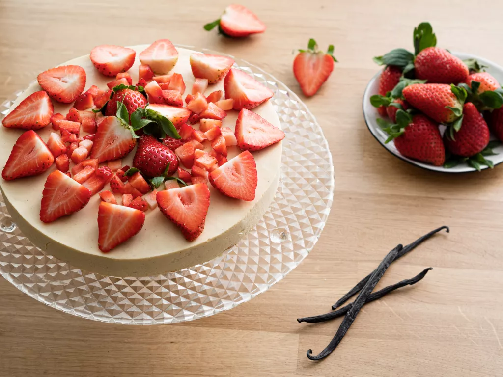 waniliowy krem bawarski udekorowany truskawkami, obok laski wanilii i talerzyk z truskawkami