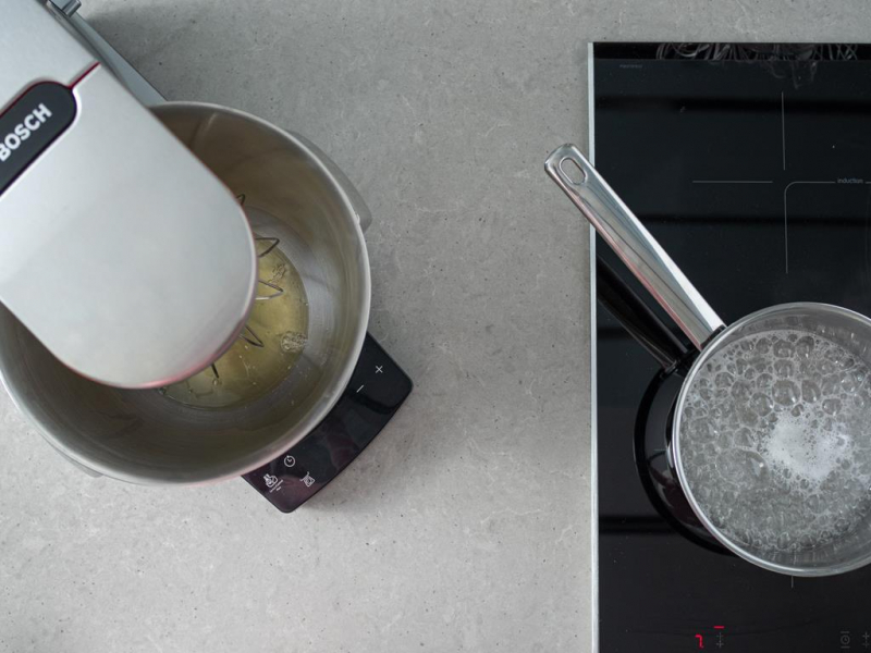 białka w misie miksera, obok na palniku gotujący się cukier z wodą