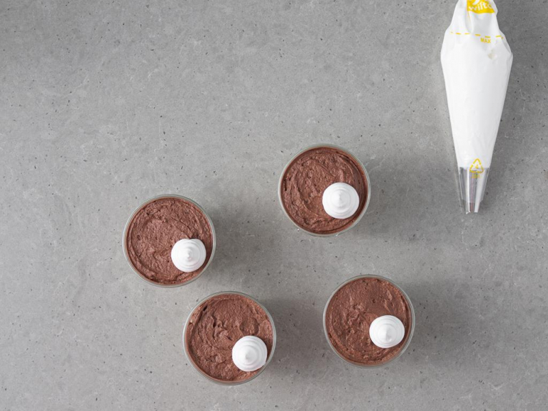 krem sułtański w pucharkach, obok rękaw cukierniczy wypełniony bezą włoską