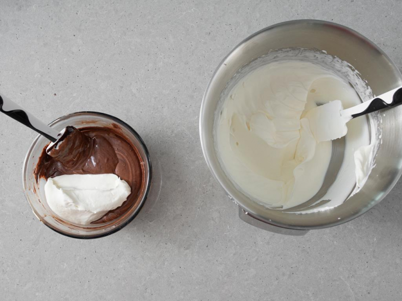 w szklanej miseczce roztopiona czekolada z częścią ubitej śmietany, obok misa miksera z ubitą na sztywno śmietaną