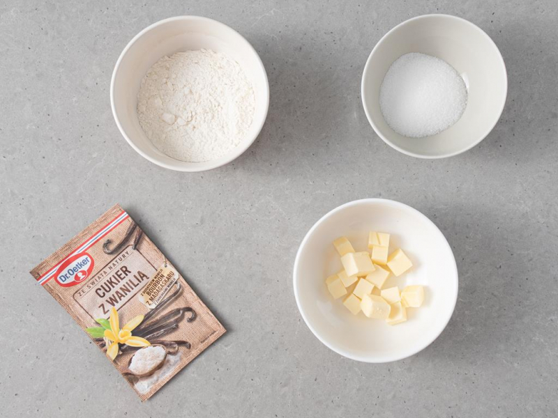 cukier waniliowy, miseczka z mąką, miseczka z cukrem, miseczka z pokrojonym w kostkę masłem