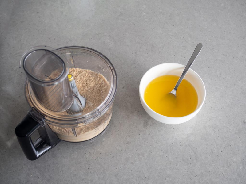 pokruszone herbatniki w malakserze i miseczka z roztopionym masłem