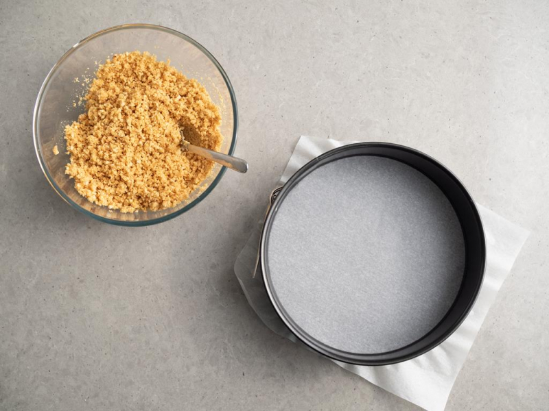 pokruszone herbatniki z masłem, tortownica wyłożona papierem do pieczenia