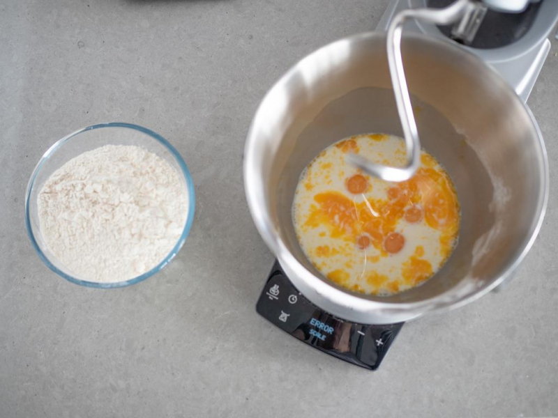 mąka wymieszana z drożdżami, obok w misie miksera mleko z cukrem i żółtkami