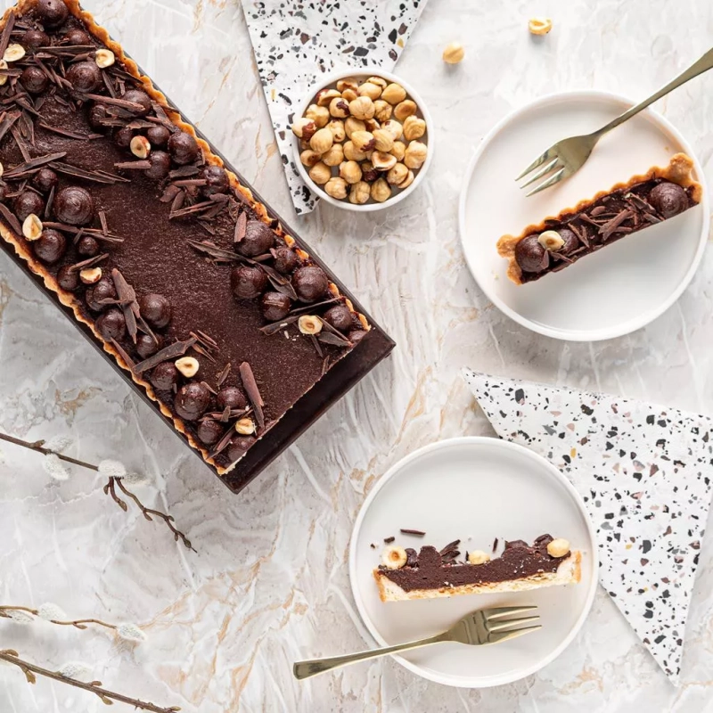 mazurek daktylowy z czekoladą i pastą sezamową w blaszce, obok pokrojony na talerzykach