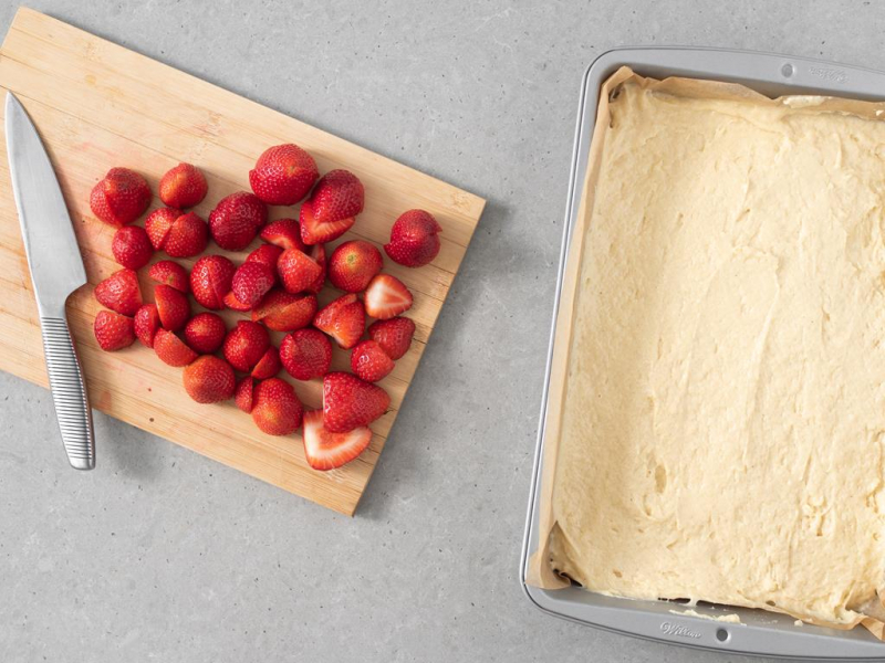 truskawki na drewnianej desce do krojenia, obok forma z ciastem