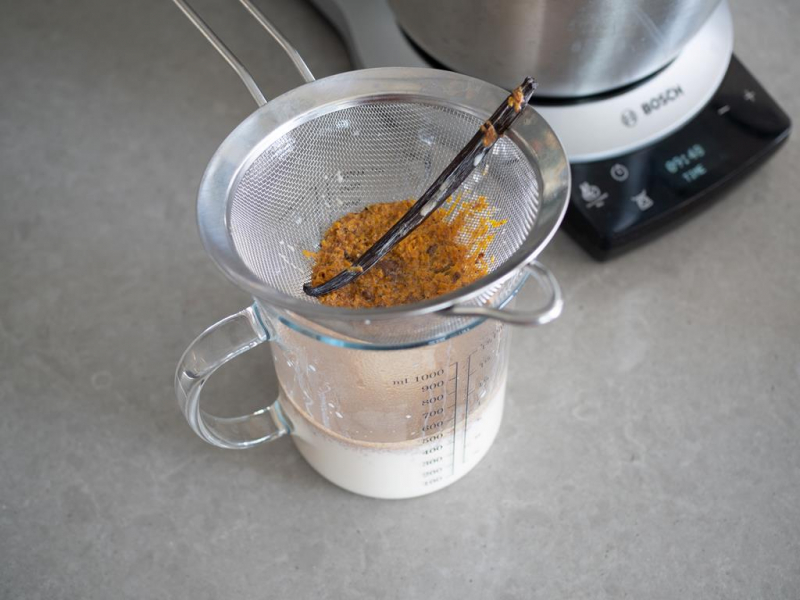 w szklanym dzbanku przecedzone mleko, na nim sitko z otartą skórką pomarańczową