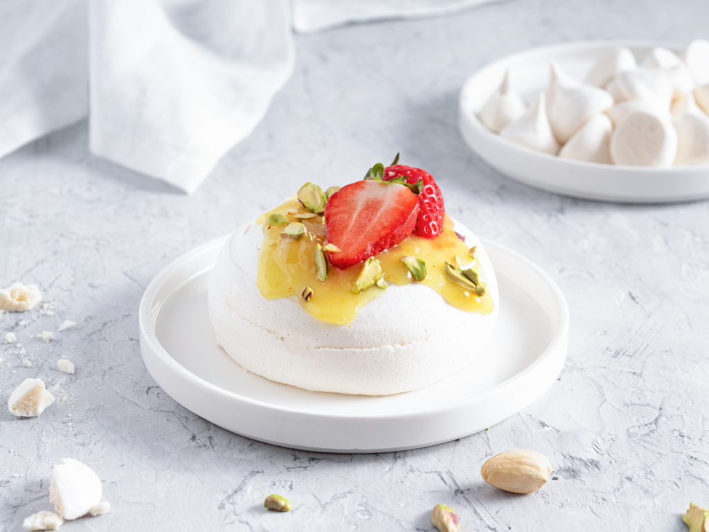 Wegańskie mini bezy z lemon curdem, truskawkami i pistacjami na białym talerzyku - Wszystkiego Słodkiego