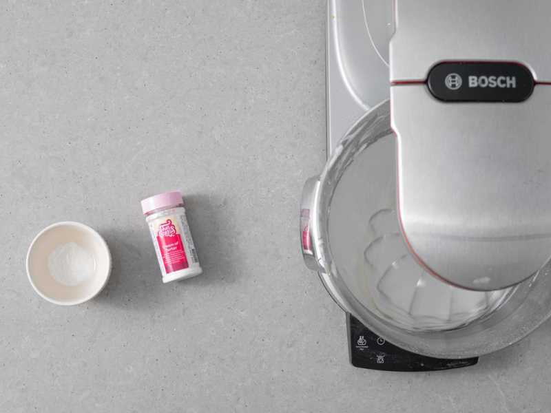 Ubijanie wegańskiej masy bezowej w robocie kuchennym. Obok w miseczce mąka ziemniaczana i szczypta soli. Obok kamień winny FunCakes.