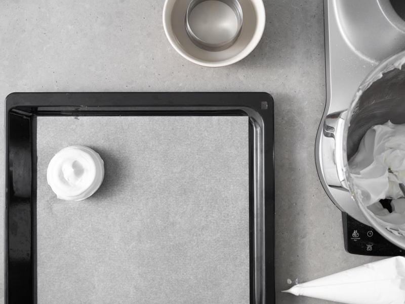 Wyciśnięta masa bezowa na blasze do pieczenia. Obok w miseczce namoczony w zimnej wodzie ring.