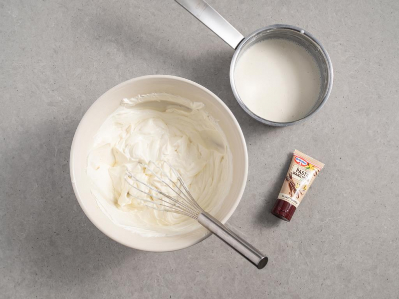 w misce masa sernikowa na ciasto pszczółka, obok rondelek z rozpuszczoną żelatyną wymieszaną z niewielką ilością masy sernikowej praz opakowanie pasty waniliowej intense od dr. oetkera