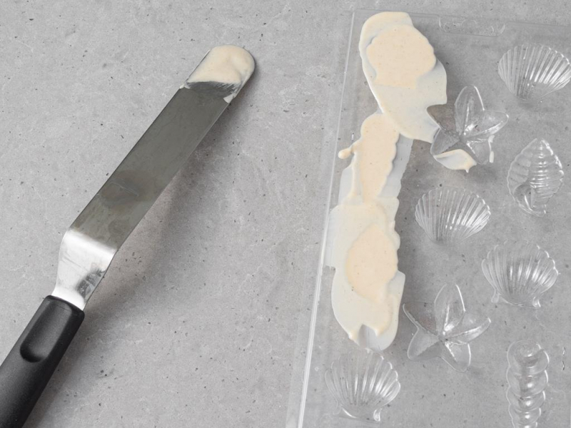 Foremka do czekoladek w kształcie muszelek, a obok szpatułka.