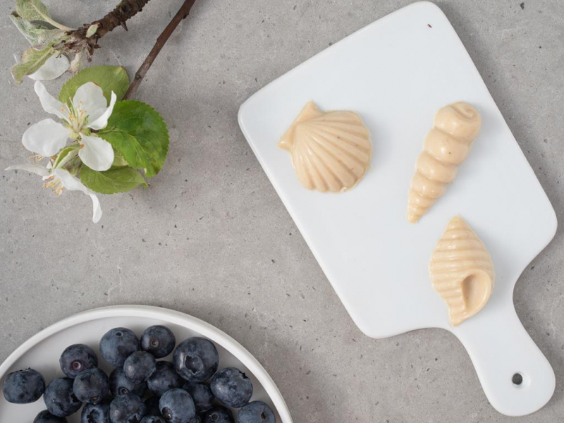 Czekoladki w kształcie muszelek na białej desce.