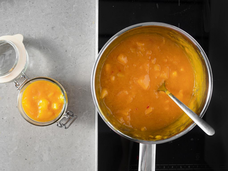 Gotowy chutney z mango i chili w garnku i przekładanie go do słoiczka.