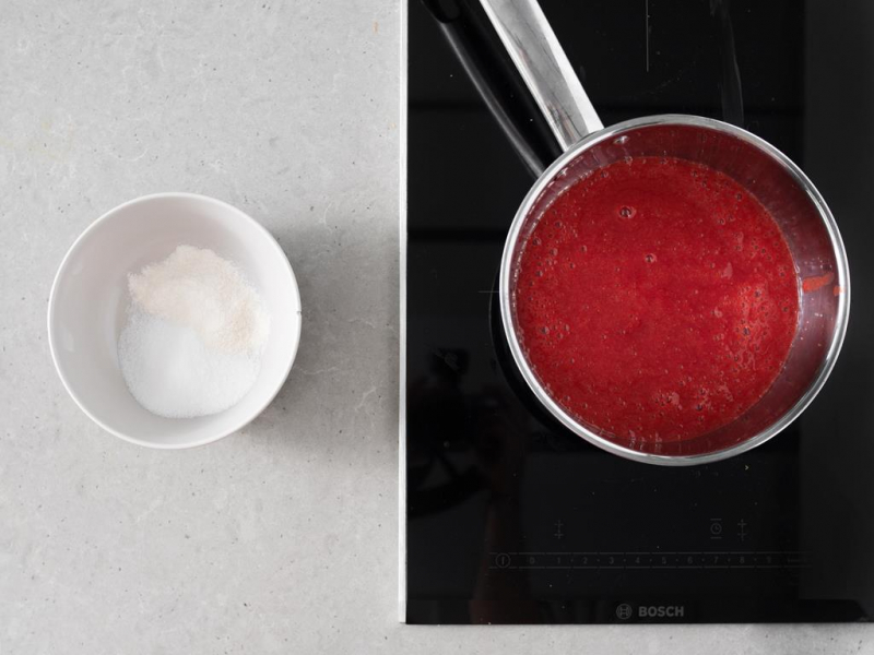 Zblendowane truskawki w garnku. Obok w miseczce cukier oraz żelfix.