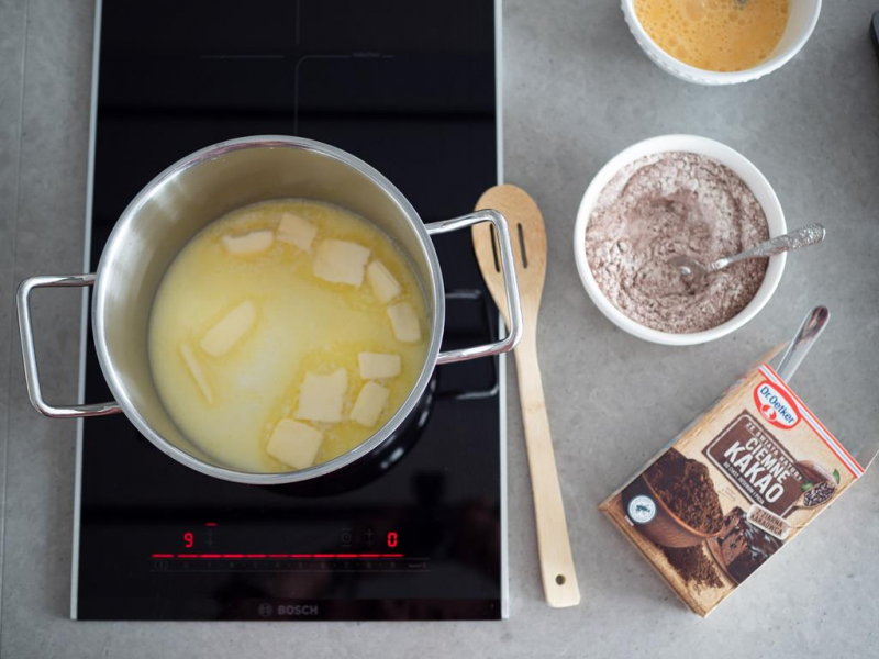 w garnku mleko z masłem na ciasto parzone, obok ciemne kakao dr. Oetkera