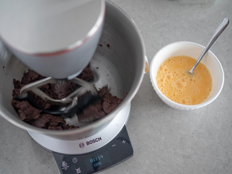 w robocie kuchennym bosch kakaowe ciasto parzone obok miseczka z jajkami