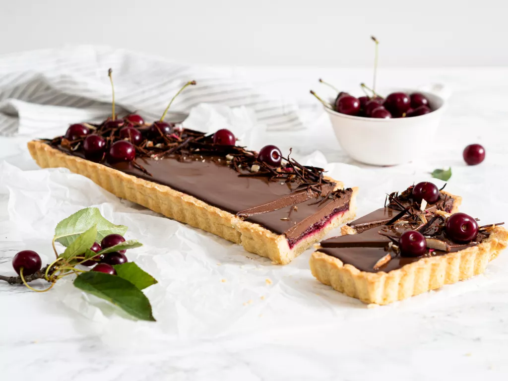 Wegańska tarta czekoladowa z wiśniami udekorowana świeżymi owocami, wiórkami z czekolady i migdałami - Wszystkiego Słodkiego