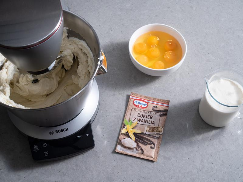 w robocie kuchennym bosch składniki na sernik baskijski: serek śmietankowy i serek mascarpone utarte z cukrem, obok w miseczce jajka, śmietanka w szklanym dzbanuszku i cukier z wanilią Bourbon Dr. Oetker