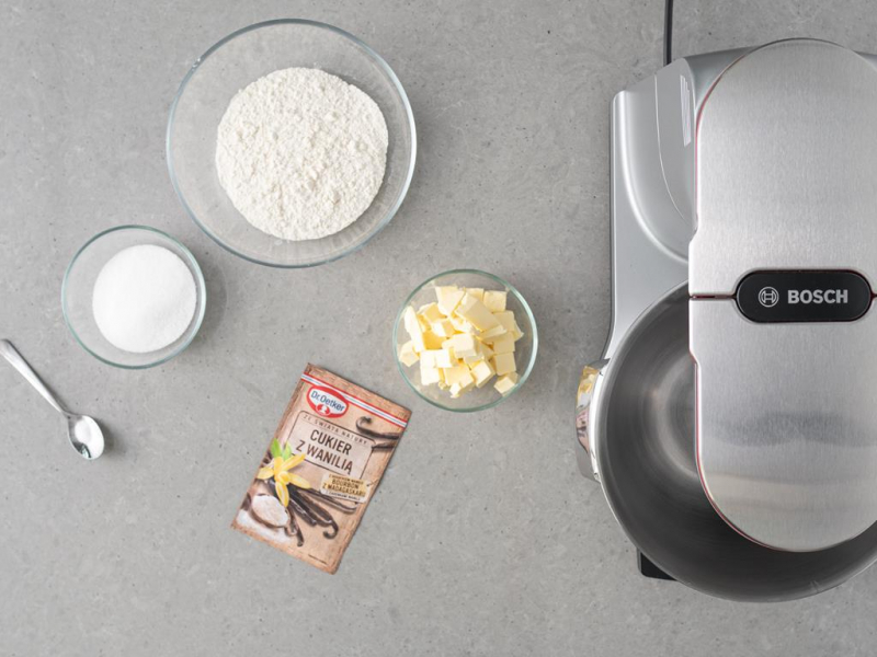 Na blacie kuchennym robot kuchenn firmy Bosch. Obok cukier z wanili膮, m膮ka pszenna, cukier, s贸l i margaryna ro艣linna.