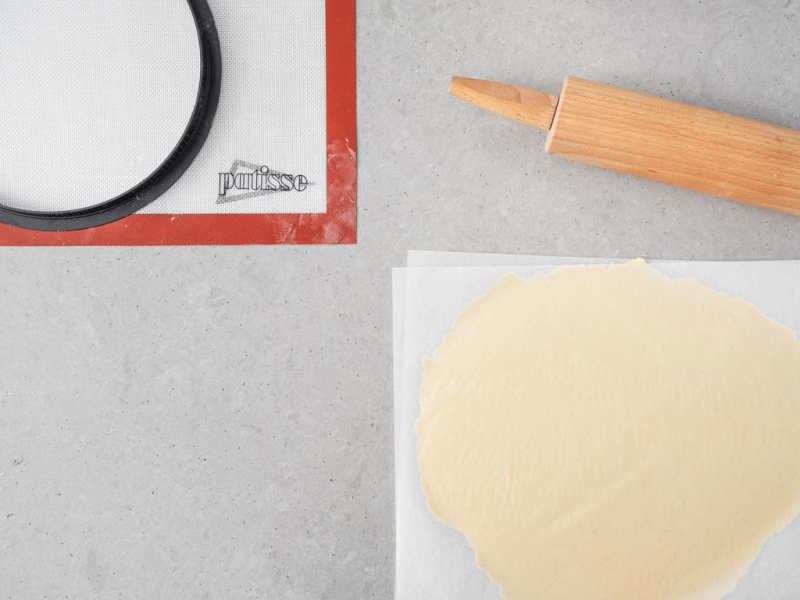 Wega艅skie ciasto kruche rozwa艂kowane pomi臋dzy dwoma arkuszami papieru.