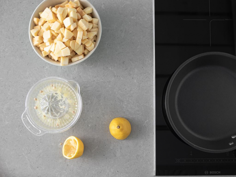 patelnia na p艂ycie indukcyjnej. Obok pokrojone w misie jab艂ka i sok z cytryny.