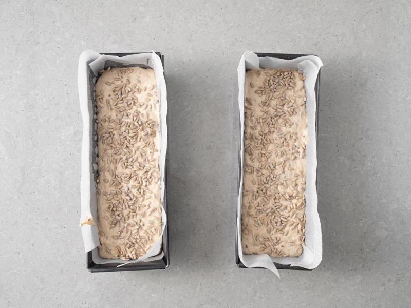 Ciasto na chleb przełożone do keksówek i posypane ziarnami słonecznika.