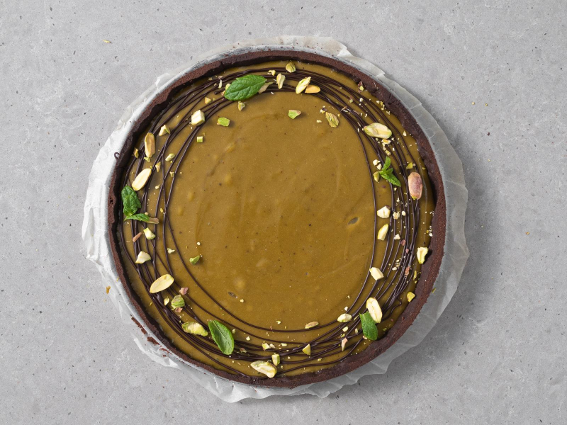 Tarta pistacjowa udekorowana czekoladą, posiekanymi pistacjami i listkami mięty.